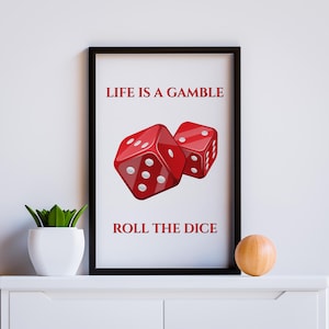 以下が含まれることがあります： 「LIFE IS A GAMBLE ROLL THE DICE」のテキストが入った額入りアートプリント。白いドットが付いた2つの赤いサイコロが特徴です。プリントは黒いフレームに入っており、白い表面に表示されています。