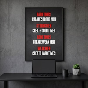 May include: A black framed poster with the text "HARD TIMES CREATE STRONG MEN, STRONG MEN CREATE GOOD TIMES, GOOD TIMES CREATE WEAK MEN, WEAK MEN CREATE HARD TIMES" in white and red. A laptop, mug, and plant sit on a black desk.