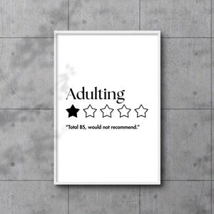 Könnte beinhalten: Ein weiß gerahmter Druck mit dem Wort "Adulting" in Schwarz, bewertet mit einem von fünf Sternen. Der Text darunter lautet "Total BS, would not recommend.", vor einer grauen Wand.