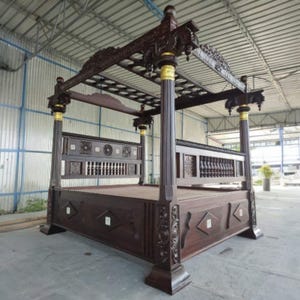 Puede incluir: Una cama con dosel de color marrón oscuro, intrincadamente tallada. La cama presenta diseños ornamentados en la cabecera y el piecero, con detalles dorados en los postes. El dosel también está detallado con patrones tallados. Un mueble llamativo.