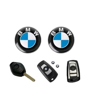 May include: A collection of BMW car accessories, including two round black and white logo emblems with a blue and white cross design, and three car keys. The keys are black and silver.