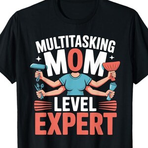 May include: Black t-shirt with a graphic design. The design features the words "MULTITASKING MOM LEVEL EXPERT" in white and red. The word "MOM" is in a large, bold font. The graphic includes a stylized figure with multiple arms holding various tools.