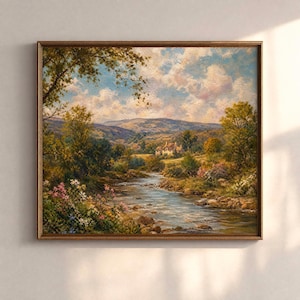 Op de afbeelding: Een ingelijst landschapsschilderij dat een serene rivierscène toont. Het kunstwerk toont een stromende rivier, weelderig groen en een schilderachtig huis genesteld tussen glooiende heuvels onder een bewolkte hemel. De lijst is warm goudbruin.