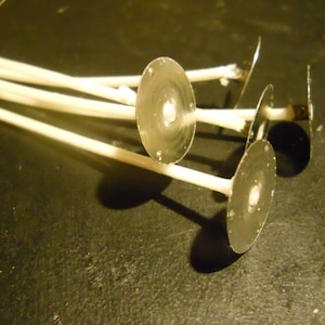May include: A close-up of several white candle wicks with metal bases. The wicks are bundled together and the metal bases are visible.