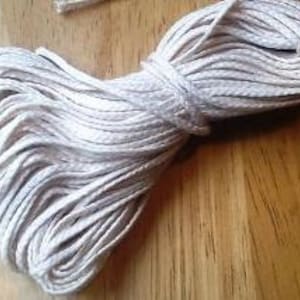May include: A close-up of a white cotton cord, wound into a coil. The cord is smooth and appears to be made of natural fibers.