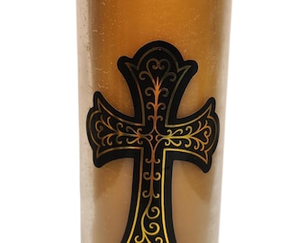May include: A tall, cylindrical candle in a clear glass jar. The candle is a warm, golden color. A black and gold decorative cross is affixed to the front of the candle. The candle is unscented.