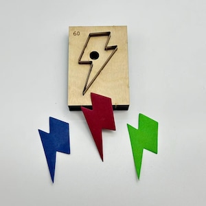 Può includere: Un utensile da taglio in legno a forma di fulmine, accompagnato da tre fulmini in feltro blu, rosso e verde. Il numero 60 è stampato sul blocco di legno. Questo strumento viene utilizzato per l'artigianato e la creazione di forme.