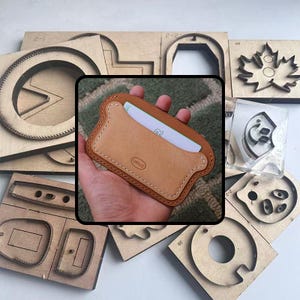 May include: A light brown leather card holder with a stitched border, held in a hand. The card holder contains a white card. Surrounding the card holder are various wooden craft templates.