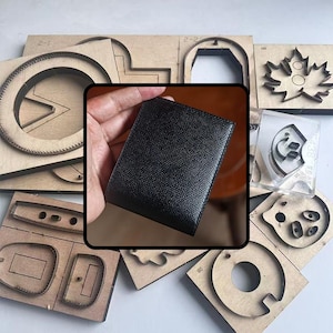 Puede incluir: Una cartera de cuero negro se sostiene en una mano, rodeada de varias formas de troquelado de madera. La cartera tiene una superficie texturizada. Las formas de madera incluyen círculos, formas de hojas y otros diseños geométricos.