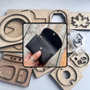 Puede incluir: Cartera de cuero negro con cierre de botón a presión, abierta para revelar el interior. Alrededor de la cartera hay varias plantillas de manualidades de madera con formas recortadas, incluyendo círculos, rectángulos y diseños de hojas.