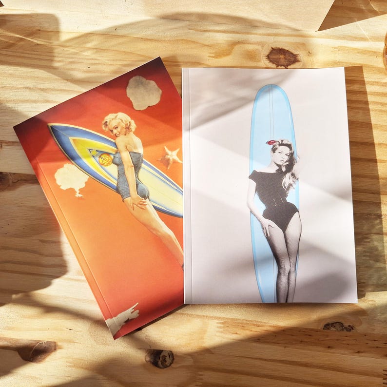 May include: Two notebooks with retro illustrations. One depicts a woman in a swimsuit with a surfboard against an orange backdrop. The other shows a woman in a black swimsuit with a blue surfboard on a white background.
