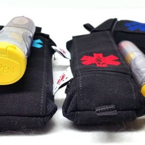 May include: Two black fabric cases with red and blue medical star symbols. Each case holds a yellow EpiPen auto-injector with a clear plastic body.