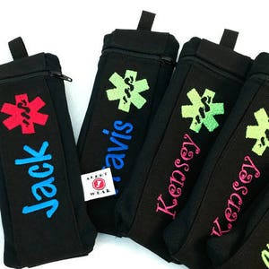 May include: Four black zippered pouches with different colored embroidered names and a red medical symbol. The pouches are labeled "Jack", "Travis", "Kensey", and "Kensey".