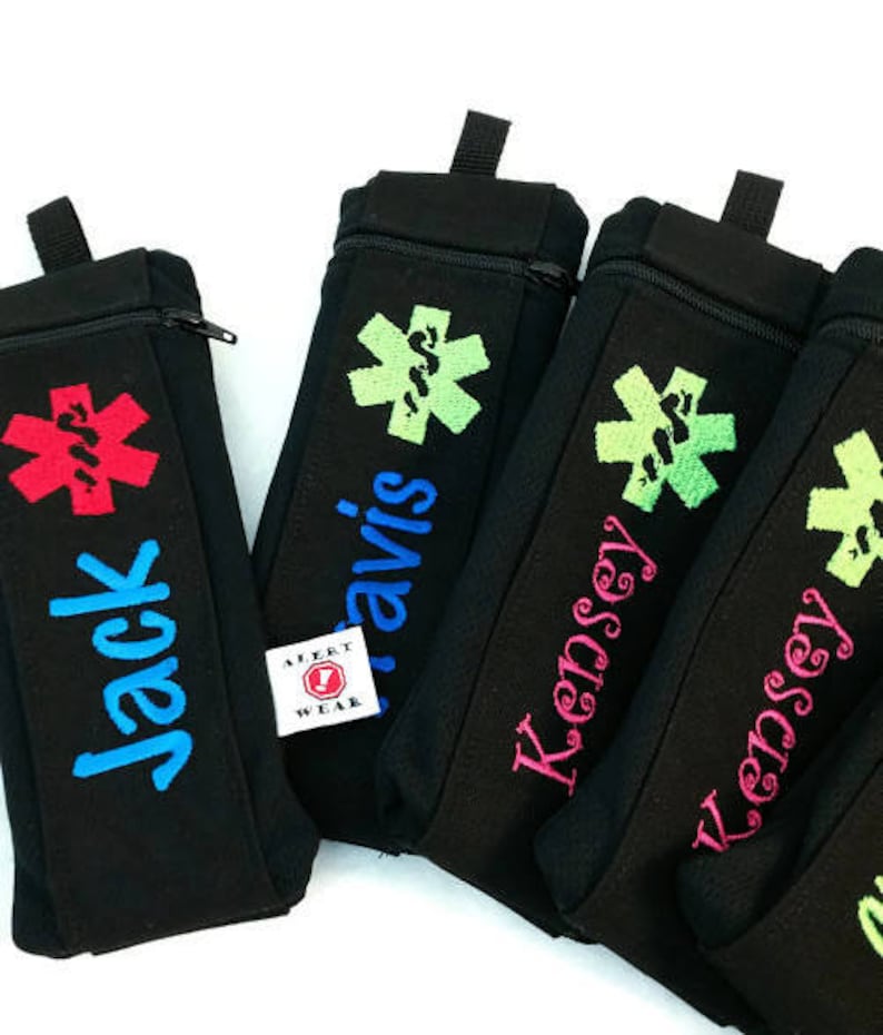 May include: Four black zippered pouches with different colored embroidered names and a red medical symbol. The pouches are labeled "Jack", "Travis", "Kensey", and "Kensey".