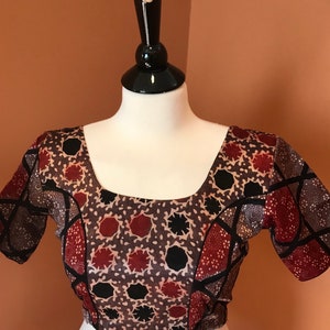 Puede incluir: Una blusa de color marrón, negro y rojo con estampado, mangas cortas y cuello redondo.