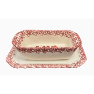 May include: A rectangular, off-white ceramic baking dish with a matching serving tray. Both pieces feature a decorative red floral pattern around the edges. The dish is placed on top of the tray.
