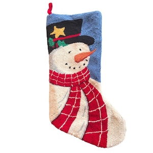 Puede incluir: Un calcetín navideño con un diseño de muñeco de nieve. El muñeco de nieve tiene un sombrero de copa negro con una estrella dorada, una nariz de zanahoria naranja y una bufanda roja. El fondo es azul.