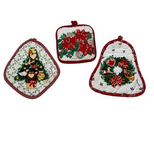 May include: Three quilted fabric pot holders with holiday themes. One is diamond-shaped with a Christmas tree, one is square with red poinsettias, and one is bell-shaped with a wreath, bells, and a rocking horse. All have red trim.