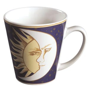 May include: A white ceramic mug featuring a dark blue background decorated with gold stars. The front of the mug displays a large, detailed illustration of a sun and crescent moon face merged together in cream and gold tones with a gold rim.