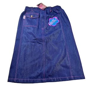 May include: A dark blue denim midi skirt featuring bright pink contrast stitching, an elastic waistband, and a single flap pocket on the upper right side. A pink and blue cloud-shaped patch with the word Hello! is attached to the front.