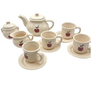 May include: A ceramic tea set in an off-white glaze featuring a hand-painted red apple motif on each piece. The set includes a teapot with a lid, a lidded sugar bowl, a creamer, and three cups with matching saucers, all with a smooth finish.