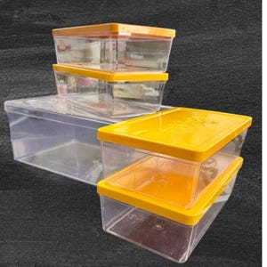 May include: A stack of clear plastic storage containers with bright yellow lids. The containers are rectangular and vary in size, with the largest one at the bottom. The lids appear to snap on securely, offering a practical storage solution.