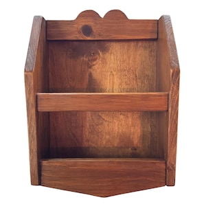 May include: A wooden wall-mounted organizer with a rich brown finish. It features a scalloped top, two shelves, and a triangular base. The organizer is designed to hold small items and has a rustic, handcrafted appearance.
