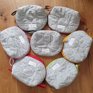 Könnte beinhalten: Eine Sammlung von sieben runden, gesteppten Stoffbeuteln mit floralen Mustern in Schwarz und Weiß. Jede Tasche hat einen unterschiedlich farbigen Reißverschluss und Griff, darunter Rosa, Rot, Gelb und Grün. Jede Tasche hat ein weißes Etikett mit Text.