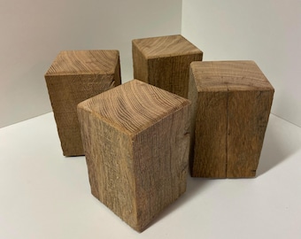 Könnte beinhalten: Vier rechteckige Holzblöcke aus natürlichem, unbehandeltem Holz. Jeder Block weist eine deutliche, sichtbare Holzmaserung mit einer hellbraunen, verwitterten Textur auf. Die Blöcke sind in einer Gruppe angeordnet und zeigen ihre massive Form.