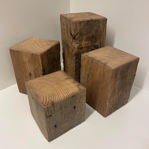 Op de afbeelding: Een set van vier rechthoekige houten blokken van verschillende hoogtes, elk met een natuurlijke bruine kleur, zichtbare houtnerfpatronen op de bovenzijden en een ruwe, verweerde textuur aan de zijkanten met duidelijke knoesten.