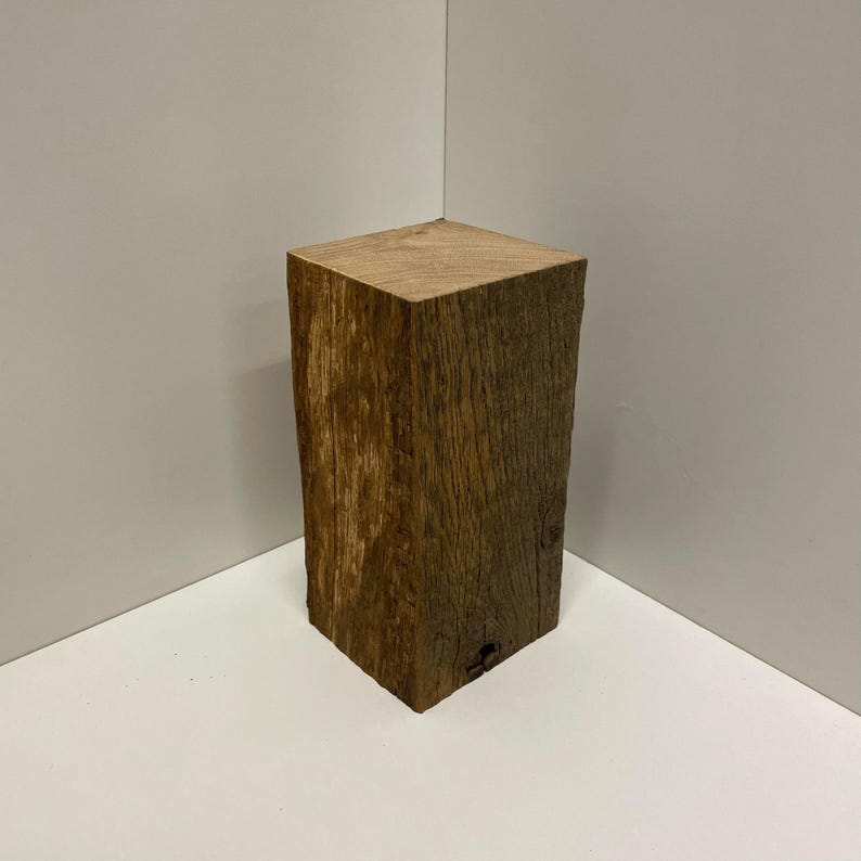 May include: A rectangular block of natural brown wood with a visible grain pattern and a rough, textured surface. The object has a flat top and vertical sides, showcasing the organic texture and variations in the wood's color and natural finish.