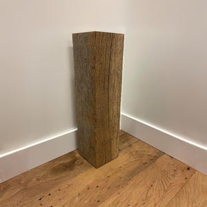 Op de afbeelding: Een hoge, rechthoekige houten pilaar met een verweerde, lichtbruine afwerking en zichtbare verticale houtnerfpatronen. Het object heeft een solide, blokvormige structuur met scherpe, strakke randen en een ruw, getextureerd oppervlak.