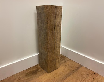Può includere: Un pilastro in legno alto e rettangolare con una finitura marrone chiaro usurata e venature del legno verticali visibili. L'oggetto ha una struttura solida a forma di blocco con bordi netti e una superficie ruvida e strutturata.