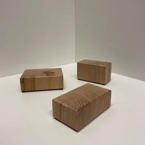 Può includere: Tre blocchi rettangolari in legno naturale color marrone chiaro. Ogni blocco presenta un motivo a venature distinto sulla superficie superiore, che mostra anelli di crescita circolari e la consistenza naturale del legno.