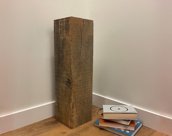 Può includere: Un pilastro in legno alto e rettangolare con una superficie marrone ruvida e usurata, caratterizzata da venature del legno visibili e un piccolo nodo. Il pilastro è posizionato verticalmente e presenta un aspetto grezzo con crepe verticali.