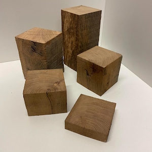 May include: A collection of five natural wood blocks of varying heights and sizes, featuring visible wood grain patterns, knots, and textured surfaces. The blocks are arranged in a group, showcasing the raw, brown, organic appearance of the timber.