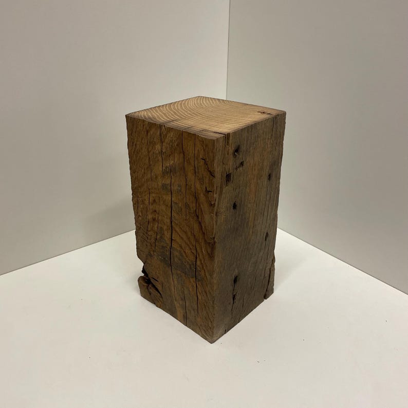 Pu&ograve; includere: Un blocco rettangolare di legno marrone scuro con un motivo a venature visibile sulla superficie superiore. I lati del blocco di legno presentano una consistenza ruvida e usurata con crepe naturali, nodi e fessure verticali.