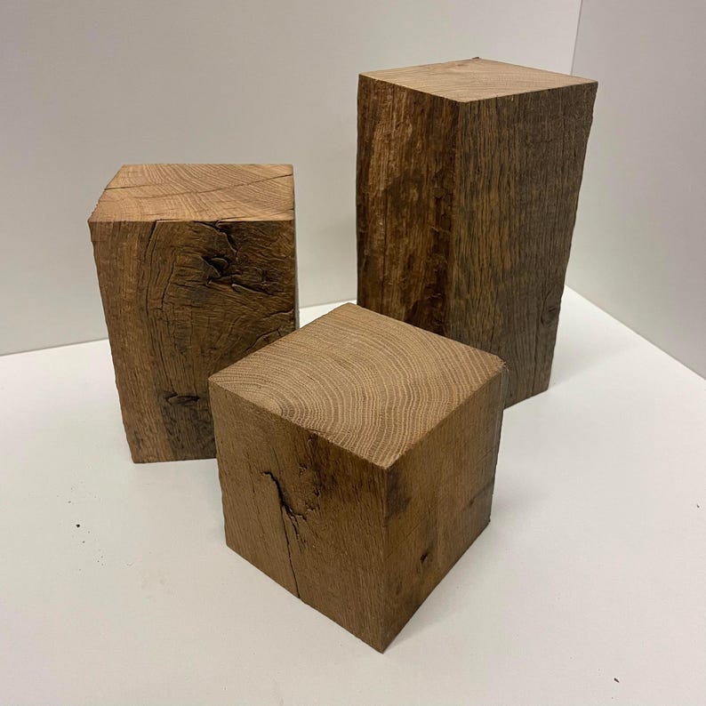May include: Three rectangular blocks of natural brown wood with visible grain patterns and rough, textured sides. The blocks vary in height and are arranged in a cluster, showcasing the organic texture and dark brown tones of the raw timber material.