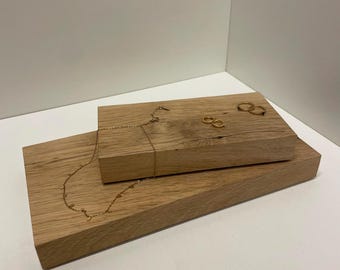 Könnte beinhalten: Zwei rechteckige, hellbraune Eichenholzblöcke, die übereinander gestapelt sind. Eine zarte goldene Halskette mit kleinen Anhängern liegt auf dem oberen Block, zusammen mit zwei kleinen goldenen Creolen auf der Holzoberfläche.