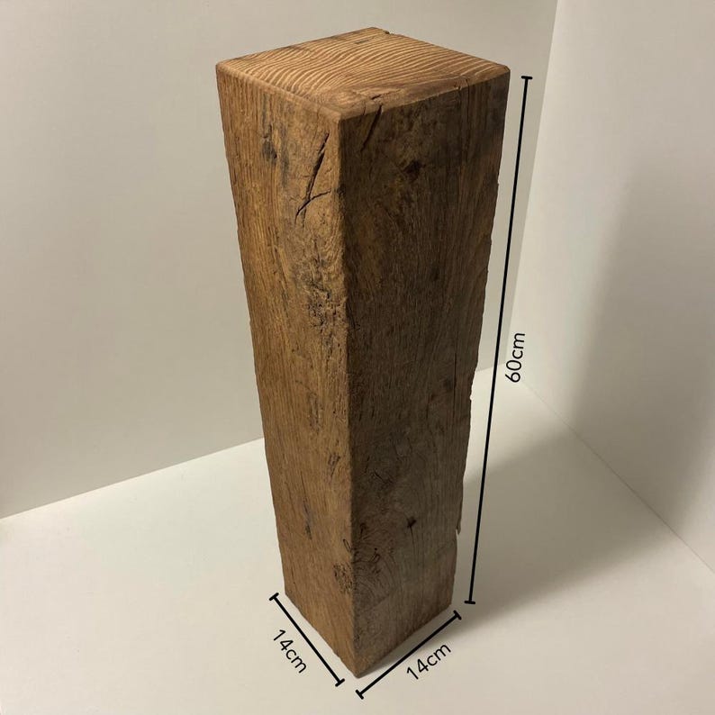 May include: A tall, square wooden pillar with a natural brown finish and visible wood grain texture. The block features rustic cracks and knots throughout its surface. It measures 60 cm in height and 14 cm by 14 cm at the base, as indicated by the lines.