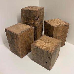 May include: Four rectangular wooden blocks of varying heights arranged in a cluster. Each block features a natural brown color with visible wood grain patterns on the top surfaces and rough, textured vertical sides showing knots and cracks.
