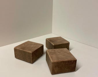 Könnte beinhalten: Drei quadratische Holzblöcke mit sichtbarer natürlicher Maserung. Jeder Block hat einen mittelbraunen Farbton und eine glatte, flache Oberseite. Die Blöcke sind in einer Gruppe angeordnet und zeigen die Holzstruktur auf allen Seiten.