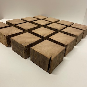 May include: A collection of sixteen square wooden blocks arranged in a four-by-four grid. Each block features a natural light brown wood grain pattern with visible texture, rough edges, and small cracks on the top surfaces and sides.