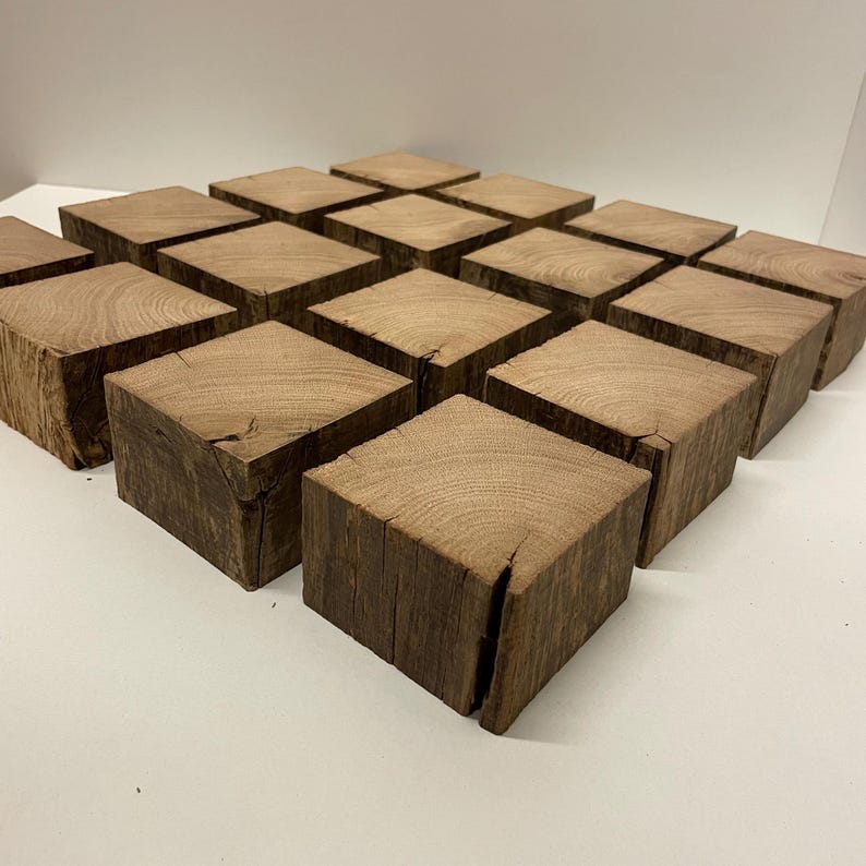 May include: A collection of sixteen square wooden blocks arranged in a four-by-four grid. Each block features a natural light brown wood grain pattern with visible texture, rough edges, and small cracks on the top surfaces and sides.