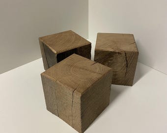 Könnte beinhalten: Drei massive Holzblöcke mit natürlicher brauner Oberfläche, jeder mit einer quadratischen Oberseite mit sichtbaren kreisförmigen Maserungen und vertikalen Rissen an den Seiten, die die rohe Textur und die organischen Linien des Holzes zeigen.