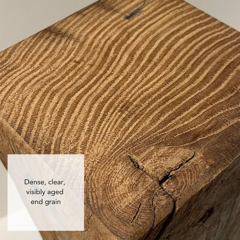 May include: A square block of natural wood featuring a prominent, dense, and visibly aged end grain pattern with light brown tones and a distinct knot. The surface displays text that reads: Dense, clear, visibly aged end grain.