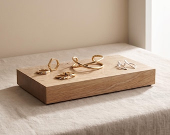 Könnte beinhalten: Eine Sammlung goldfarbener Schmuckstücke, bestehend aus einem sechseckigen Ring, zwei schlichten Ringen, einem überkreuzten Armreif und einem Paar silberfarbener Ohrringe, angeordnet auf einem rechteckigen Holzblock.