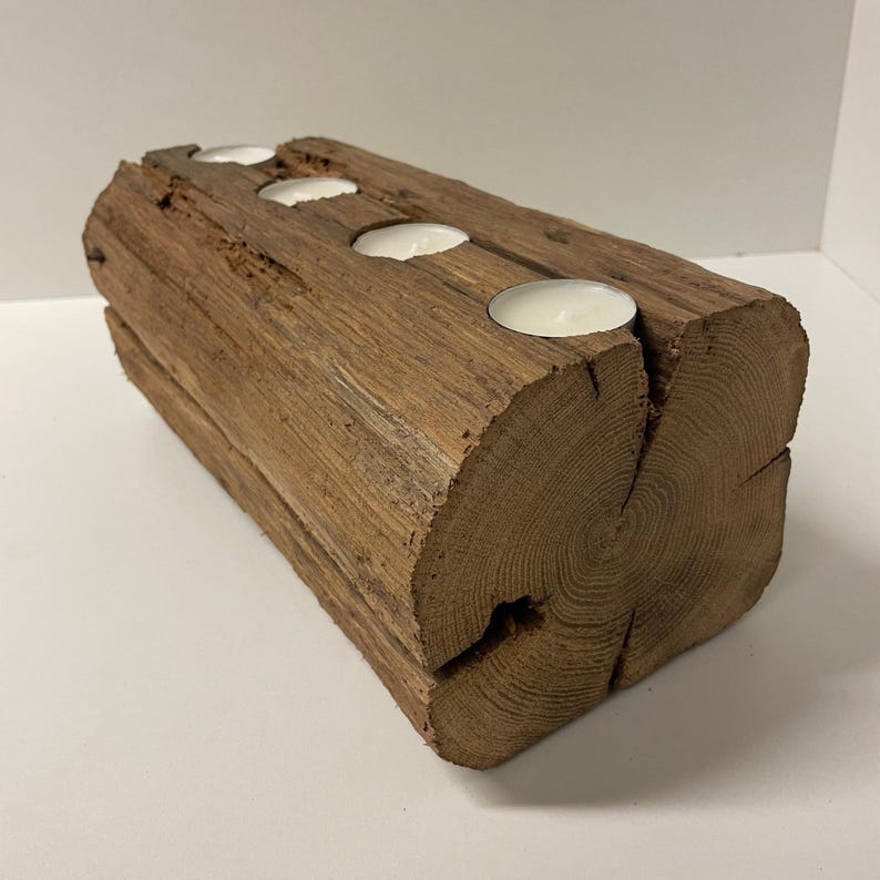 May include: A rustic wooden candle holder with three circular indentations holding white tea light candles. The candle holder is made from a section of a log, showcasing the natural wood grain and texture. The wood is a warm brown color.