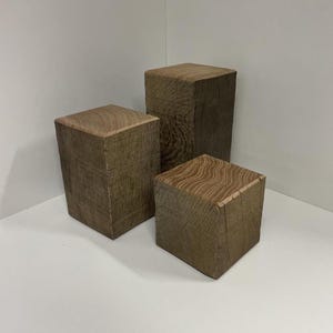 Peut inclure: Trois blocs de bois rectangulaires de hauteurs variables disposés en groupe. Chaque bloc présente une teinte brune naturelle avec des motifs de grain de bois visibles sur les surfaces supérieures et les côtés verticaux, offrant une finition brute.