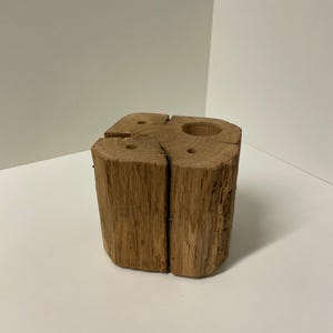 May include: A rustic, square wooden candle holder with a natural, light brown finish. The holder features a large circular opening and several smaller holes for candles. The wood grain is visible, adding to its natural aesthetic. The candle holder is a decorative item.